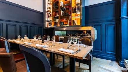 Salle de restaurant élégante de l’Hôtel Continental Reims, avec table dressée, chaises raffinées et grande bibliothèque lumineuse en arrière-plan.